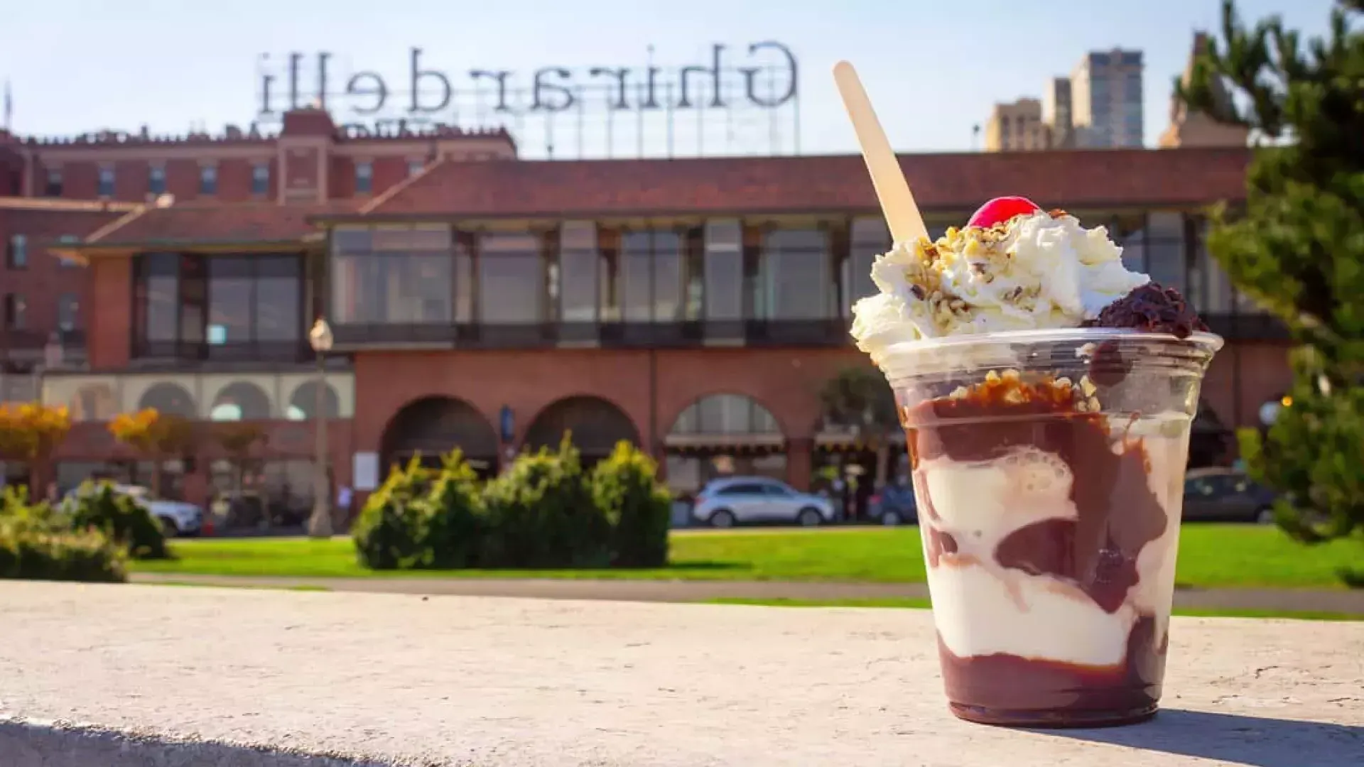 Un helado de chocolate se encuentra en primer plano con la plaza Ghirardelli al fondo.